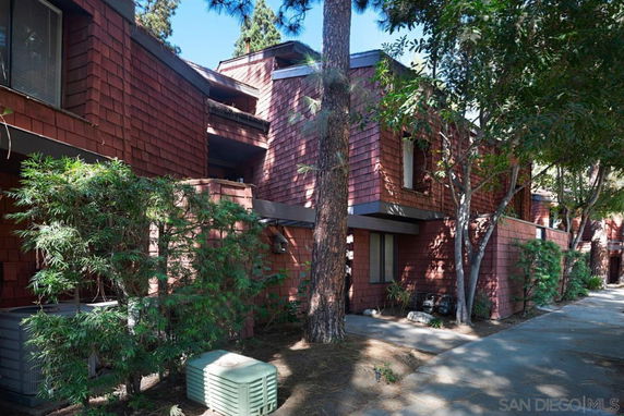 Front view of a multi-story building with textured red siding and surrounding trees.