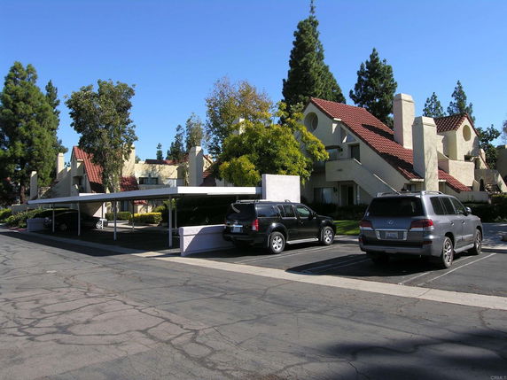 Covered parking area in front of a residential building with red-tiled roofs.