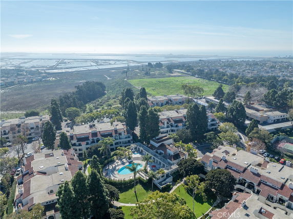 Aerial view of a residential complex with multiple buildings, a central swimming pool, and surrounding greenery, overlooking expansive wetland and water areas in the distance.