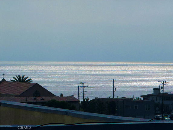 Panoramic view of the ocean with rooftops and power lines in the foreground.