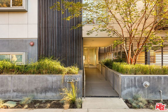Front view of a modern building entrance with a path and surrounding greenery.