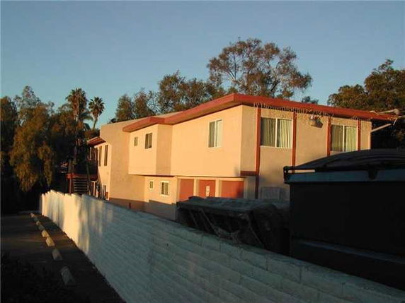 Side view of a two-story residential building with light-colored exterior walls and a flat roof.