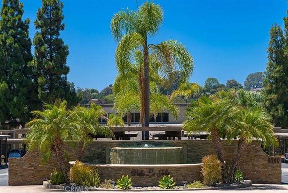 Front view of a building with surrounding palm trees and a water fountain.