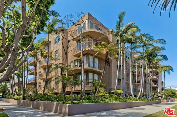 Front view of a multi-story apartment building with several balconies and palm trees surrounding it.