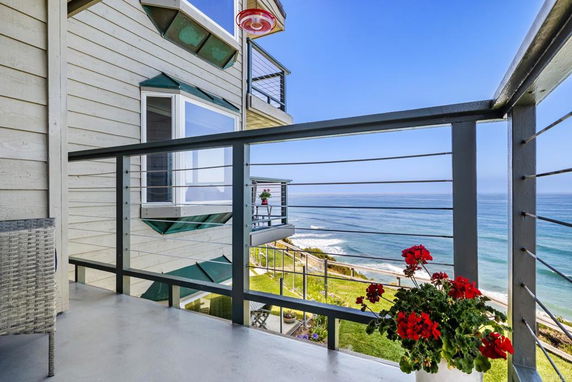 Ocean view from a balcony with railing and flower pot.