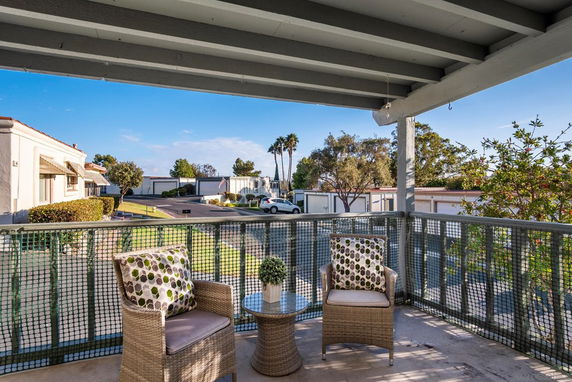 Balcony with chairs overlooking a residential area with houses and greenery.