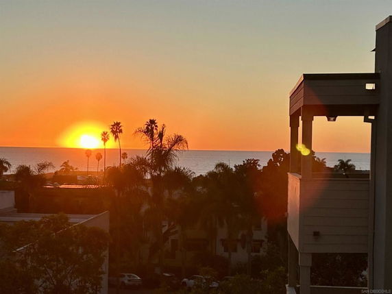 View of the ocean and sunset with palm trees and part of a building
