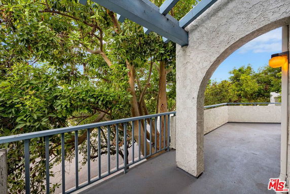 Outdoor area with arched walls and railing, overlooking trees.