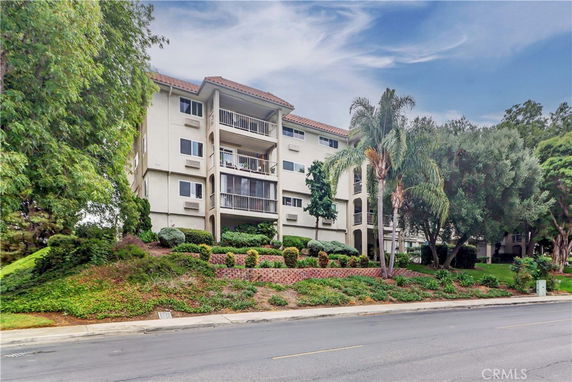 Front view of a multi-story apartment building with balconies and a landscaped garden.