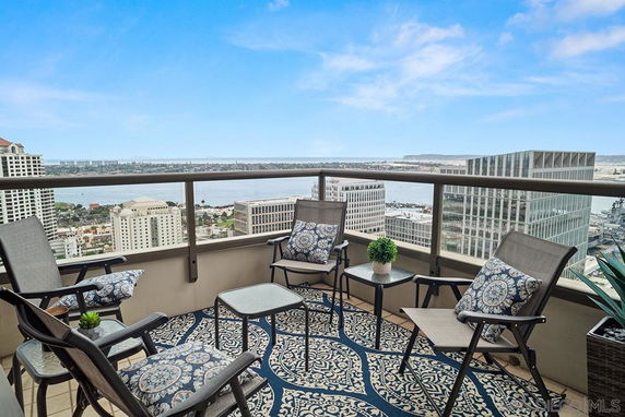 Outdoor seating area on a high-rise building balcony with cityscape and water views.