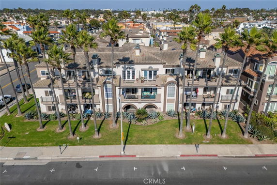 Front view of a multi-story residential building with balconies and palm trees.