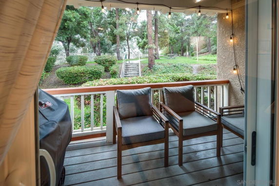 View from a covered deck with seating, overlooking a garden area with trees and shrubs.