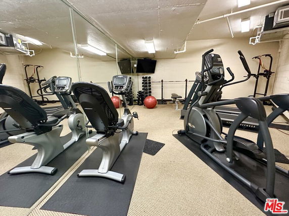 Indoor gym with exercise equipment and mirrored walls.