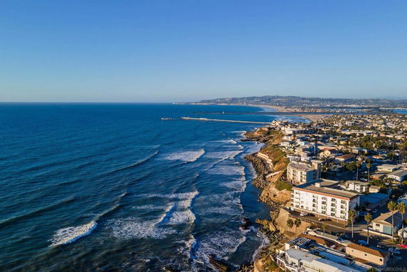 Panoramic view of a coastal area with buildings along the shoreline and a pier extending into the ocean.