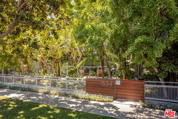 Front view of a modern building with extensive greenery and a metal fence.
