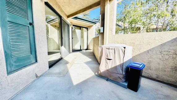 Outdoor view of a patio area with sliding glass doors and a covered appliance.