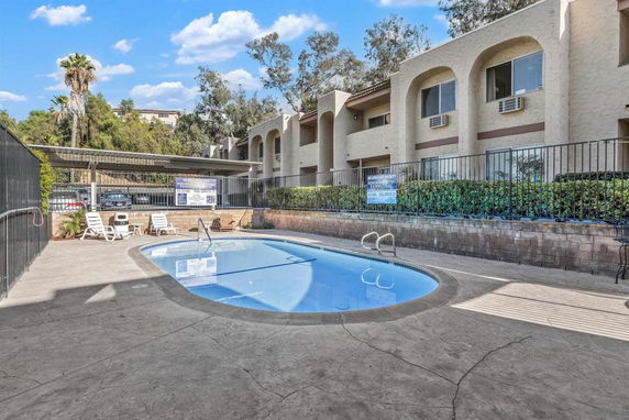 Outdoor swimming pool area with a multi-story residential building in the background.