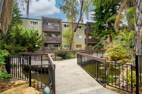 Front view of a multi-story building with balconies and a walkway, surrounded by trees.