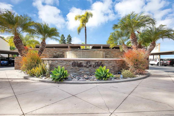 Front view of a building with a stone facade and curved entrance wall, featuring palm trees and a circular driveway.