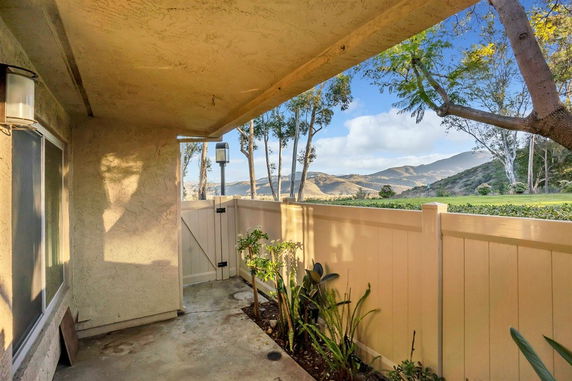 Patio area with view of hills and trees beyond a fence.