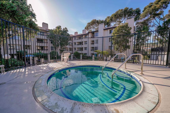 Outdoor hot tub surrounded by metal railing, with multi-story buildings in the background.