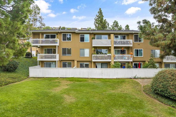 Front view of a three-story residential building with balconies and a white fence.
