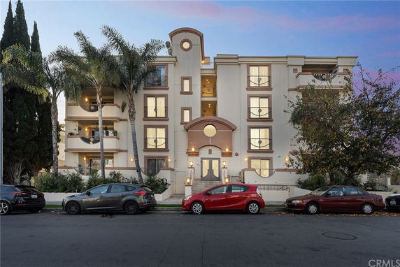 Front view of a multi-story residential building with balconies and palm trees.