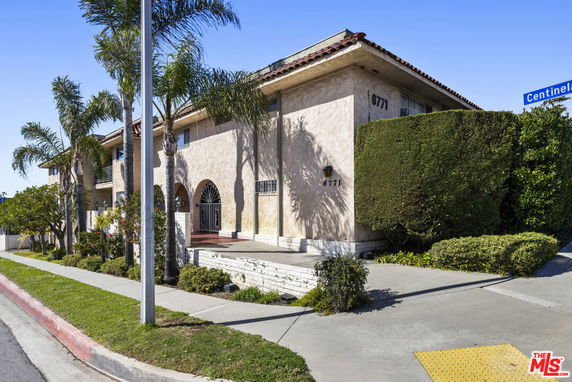 Front view of a multi-story building with arched entrance and palm trees.