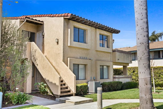 Front view of a two-story house with external staircase and tan stucco exterior.