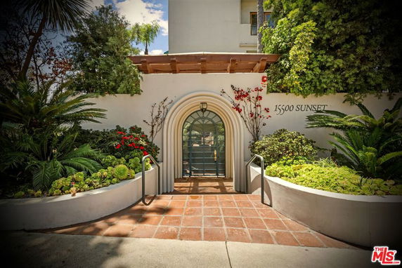 Front view of a building entrance with an arched doorway and surrounding plants.