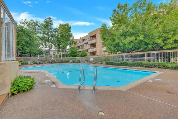 Outdoor swimming pool with surrounding trees and nearby residential buildings.