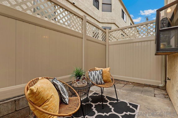 Small outdoor patio area with a fence and two wicker chairs with cushions.