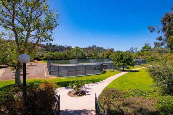 View of a tennis court surrounded by greenery and trees.