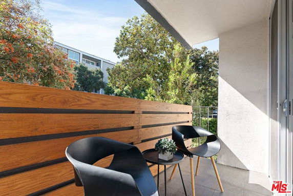 Outdoor balcony with chairs and a small table, overlooking trees and an adjacent building.