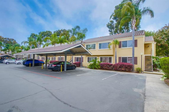 Outdoor parking area with covered parking spaces in front of an apartment building.