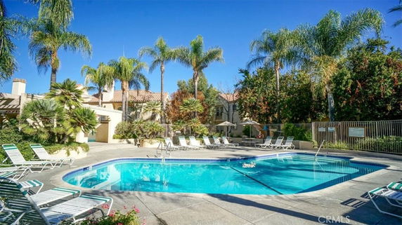 Outdoor swimming pool with surrounding lounge chairs and palm trees.