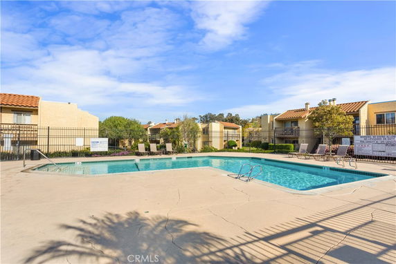 Outdoor swimming pool area surrounded by residential buildings with terracotta roofs.