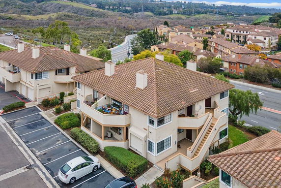 Aerial view of a residential area with multi-story buildings having tiled roofs, surrounded by roads and greenery.