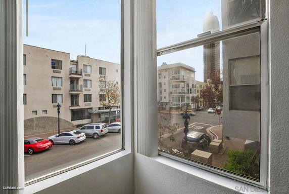 View from a window overlooking a street with cars parked and nearby buildings.
