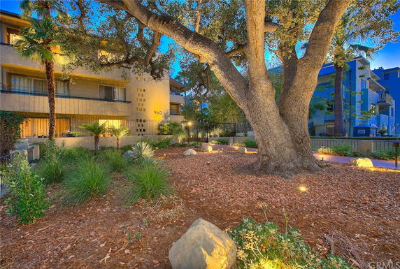 Front view of a multi-story residential building with balconies, surrounded by trees and landscaping.