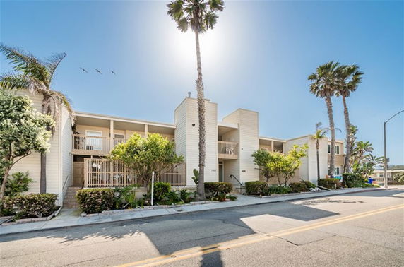 Front view of a two-story building with balconies and palm trees.