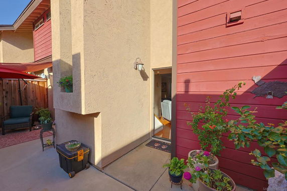 Partial view of a two-story building with stucco and wood siding, featuring a small entrance area with plants.