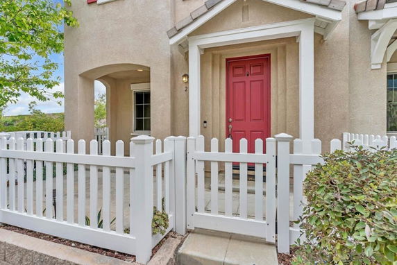 Front view of a two-story house with a red door and a white picket fence.
