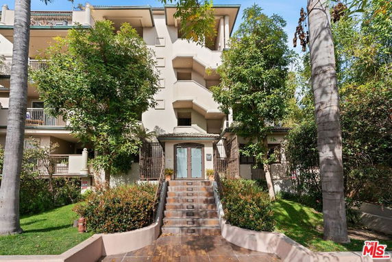 Front view of a multi-story apartment building with trees and landscaped entrance.