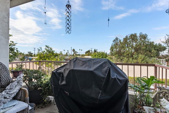 View from a balcony with outdoor furniture and potted plants, overlooking trees and open space.