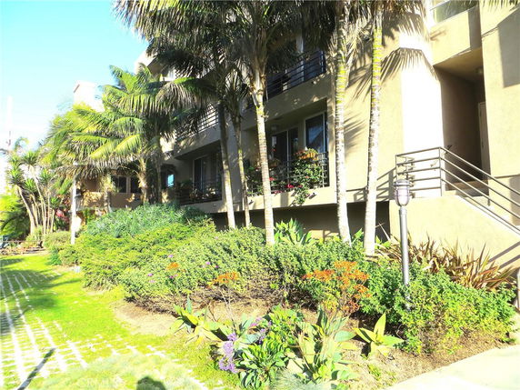 Front view of a multi-story building with balconies surrounded by lush greenery.