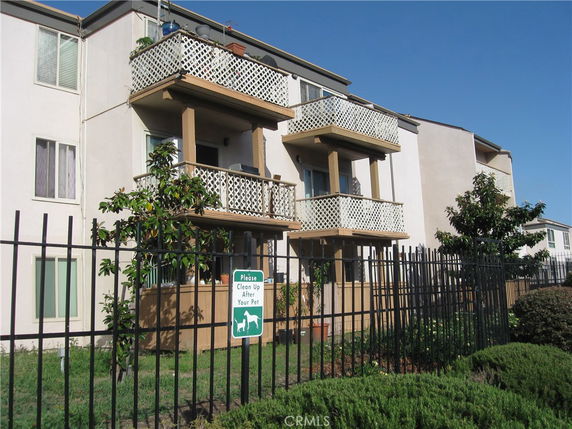 Front view of a multi-story building with balconies and a surrounding fence.