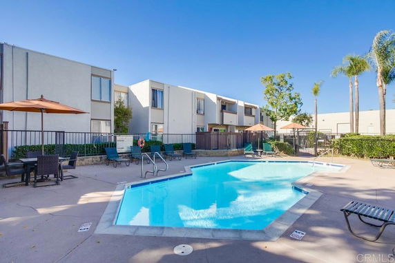 Outdoor swimming pool area with lounge chairs and umbrellas surrounded by residential buildings.