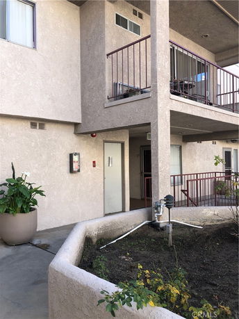View of a building entrance with a balcony and planted area.