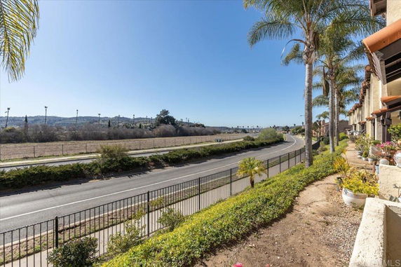 View of a road and landscaped area with palm trees and hilly background.